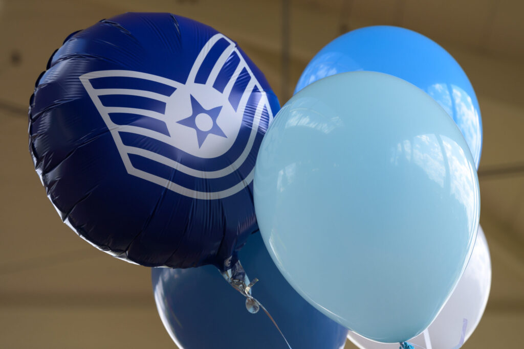 Balloons featuring the techincal sergeant insignia float under the roof of an outdoor pavillion.