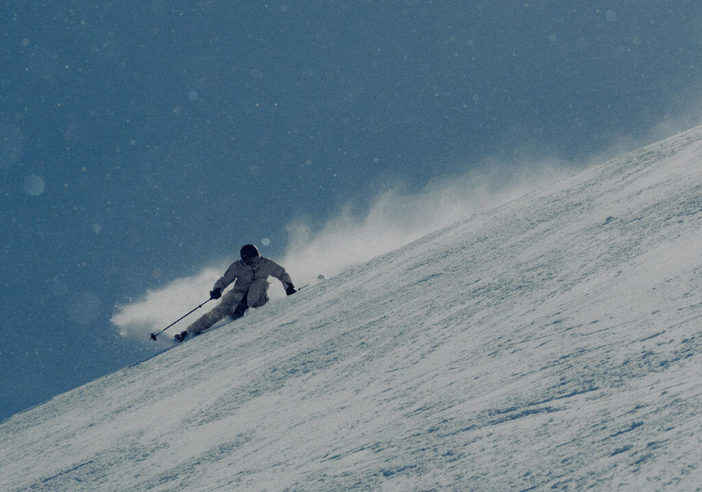 Skier in a dynamic turn on a powder slope with snow spraying behind them